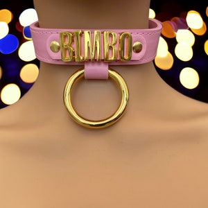 May include: Pink leather choker with a gold metal ring and the word "BIMBO" spelled out in gold letters.