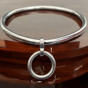 May include: A silver metal choker necklace with a large, round ring pendant.