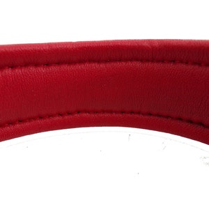 May include: Close-up of the underside of a red leather dog collar. The collar is stitched with white thread.