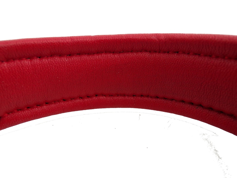 May include: Close-up of the underside of a red leather dog collar. The collar is stitched with white thread.