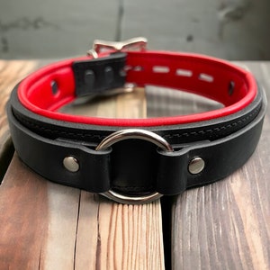 May include: Black leather collar with a red lining and a silver metal ring.