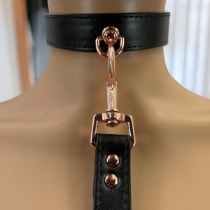 May include: Black leather choker with a rose gold metal clasp and a matching strap.