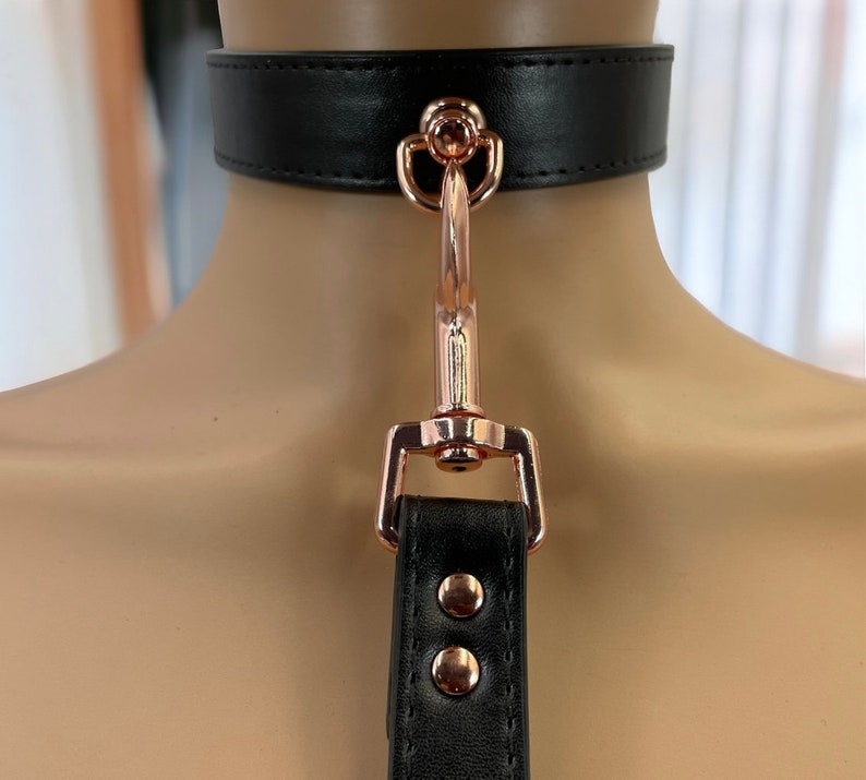 May include: Black leather choker with a rose gold metal clasp and a matching strap.