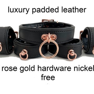 May include: Black leather collar and cuffs set with rose gold hardware. The collar is padded and has a D-ring. The cuffs are simple and have a single ring. "luxury padded leather rose gold hardware nickel free" is written below the set.