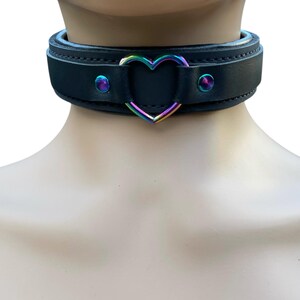 May include: Black leather choker with a rainbow heart-shaped metal ring. The choker has two silver studs on each side.