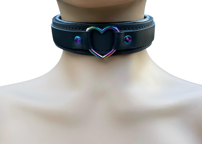 May include: Black leather choker with a rainbow heart-shaped metal ring. The choker has two silver studs on each side.