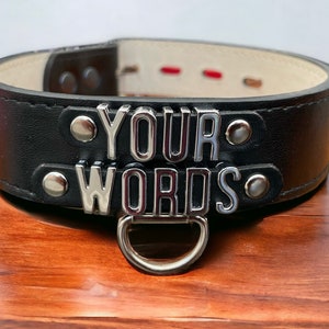 Może przedstawiać: Czarny skórzany kołnierz z srebrnymi metalowymi akcentami i napisem "YOUR WORDS".