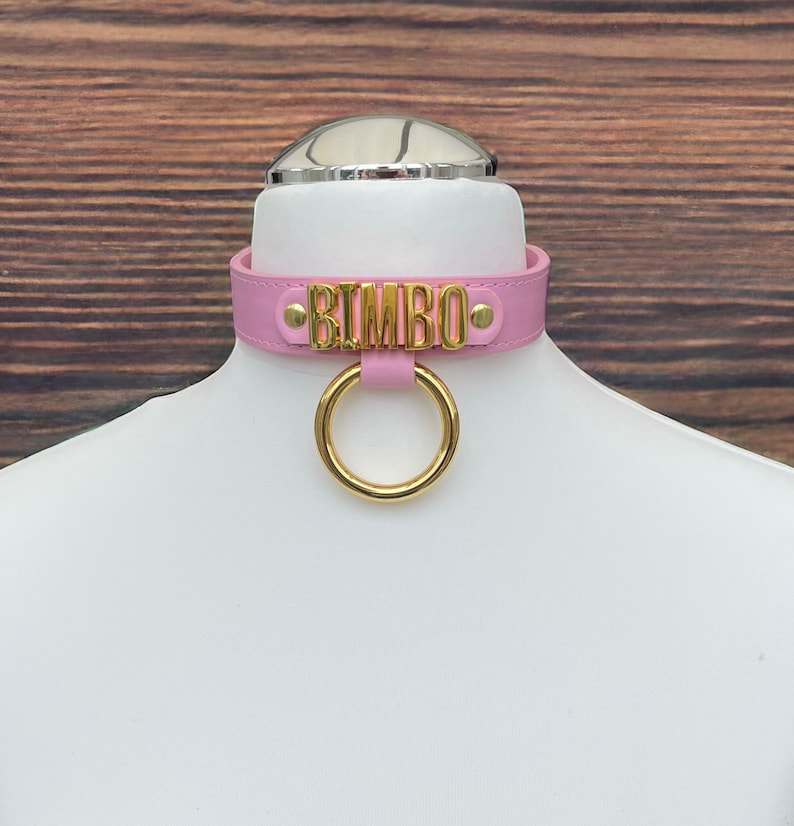May include: Pink leather choker with a gold metal ring and the word "BIMBO" in gold lettering.
