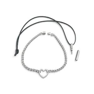 Könnte beinhalten: Eine silberfarbene Metallkettenhalskette mit einem zentralen herzförmigen Anhänger. Die Halskette enthält eine schwarze Kordel mit einem kleinen zylindrischen Metallaufsatz und einer separaten passenden Metallkappe, was ein modulares Design zeigt.