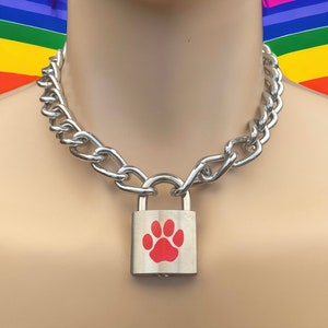 Puede incluir: Un collar gargantilla de cadena plateada con un candado plateado con un diseño de huella de pata roja.