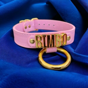 May include: Pink leather choker with a gold metal ring and the word "BIMBO" spelled out in gold letters.