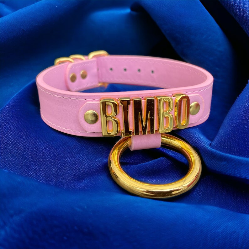 May include: Pink leather choker with a gold metal ring and the word "BIMBO" spelled out in gold letters.