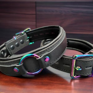Halsband i äkta läder I Chokerhalsband Svart vadderat läder I 30 mm brett 30 mm O-ring i mitten skimrande metalldetaljer regnbågsdetaljer regnbågschoker
