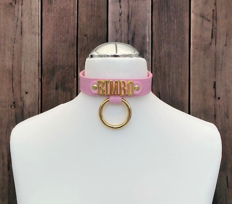 May include: Pink leather choker with a gold metal ring and the word "BIMBO" in gold lettering.
