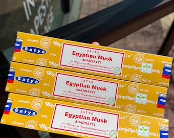 Può includere: Tre scatole rettangolari gialle di bastoncini di incenso Satya Egyptian Musk agarbatti. Ogni scatola presenta il marchio Satya in un ovale blu, il testo Egyptian Musk Agarbatti in rosso e vari loghi circolari e dettagli testuali.