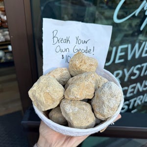 May include: A white bowl filled with beige geode stones. A sign reads "Break Your Own Geode! $10"