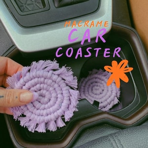 May include: Two round, light purple macrame car coasters with a fringed edge. The text MACRAME CAR COASTER is written in orange and purple above the coasters, accompanied by an orange star-shaped graphic.