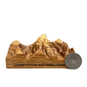 Może przedstawiać: Drewniany model pasma g&oacute;rskiego Parku Narodowego Grand Teton. Model jest mniej więcej wielkości 25 groszowej monety.