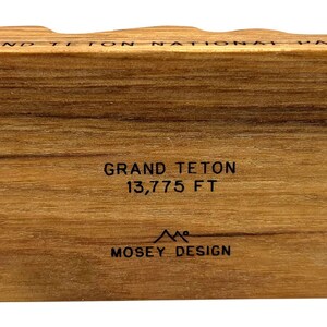 Może przedstawiać: Drewniany blok z tekstem "Grand Teton National Park" i "Grand Teton 13,775 FT" oraz logo "Mosey Design".