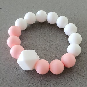 May include: A pink and white silicone teething bracelet with a white square bead. The bracelet is made of soft, chewable silicone and is designed for babies and toddlers.