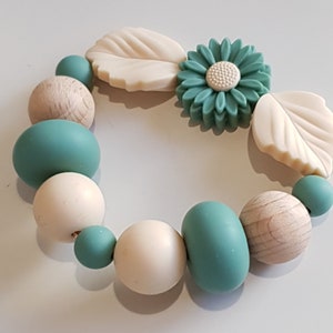 May include: A teal and cream silicone and wooden bead bracelet with a flower charm and leaf charms.