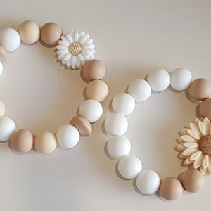 May include: Two silicone bracelets with white and beige beads and flower charms. The bracelets are made of soft, flexible silicone and are perfect for babies and toddlers.