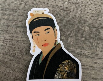 May include: A sticker featuring a stylized illustration of a person in traditional Asian attire. The person has a serious expression, wearing a black hat with gold trim and a decorative bird. The outfit is black with gold accents.