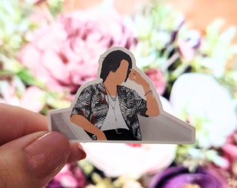 Puede incluir: Una pegatina que representa a una persona con una camisa con estampado tropical en blanco y negro, pantalones negros y collares. La pegatina tiene un borde blanco y se sostiene frente a un fondo floral borroso.