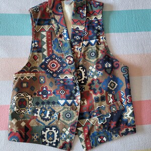 May include: A sleeveless vest with a geometric pattern in shades of brown, blue, red, and white. The vest has a collar and a button closure.