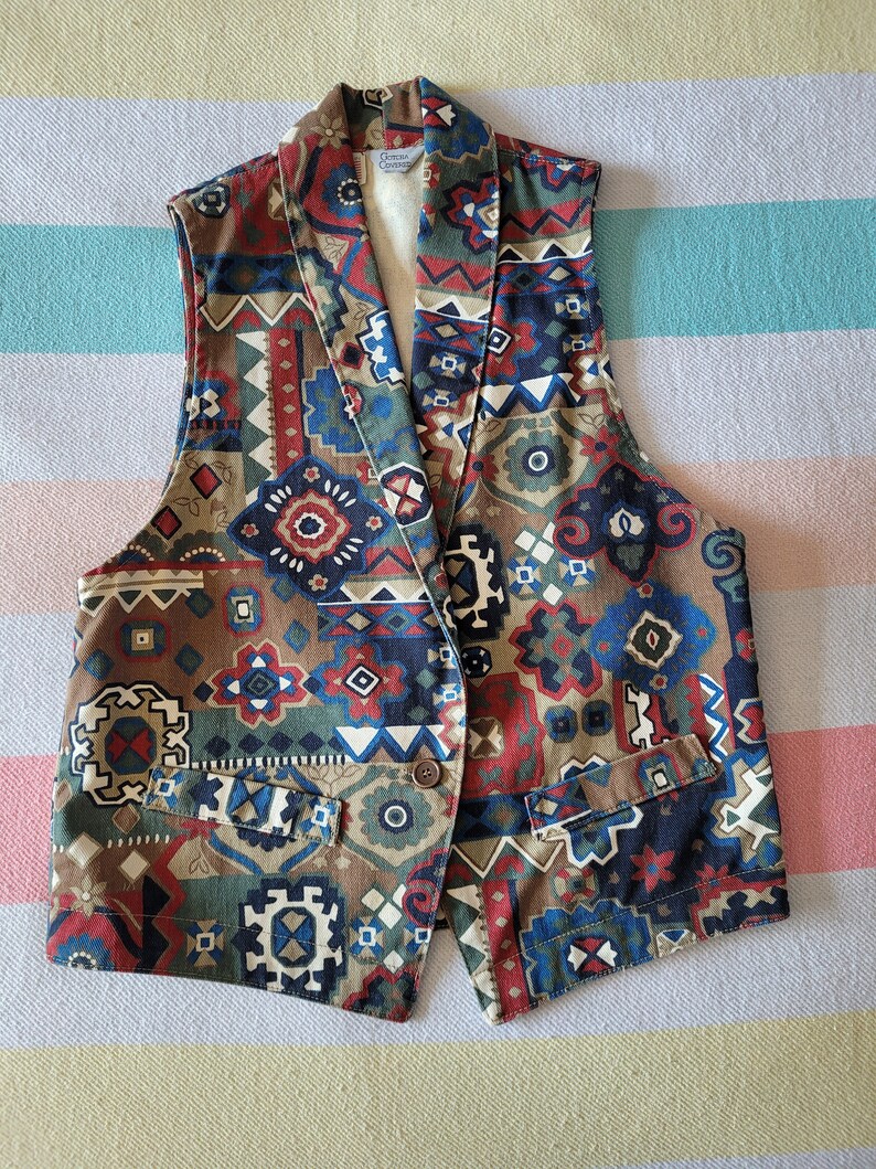 May include: A sleeveless vest with a geometric pattern in shades of brown, blue, red, and white. The vest has a collar and a button closure.