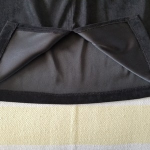 May include: Black velvet skirt with a black lining and a black hem. The skirt is turned inside out to show the lining.