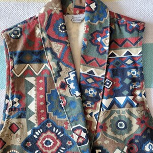 May include: A sleeveless vest with a geometric pattern in shades of brown, red, blue, and white. The vest has a large collar and a label that reads "Gotcha Covered".