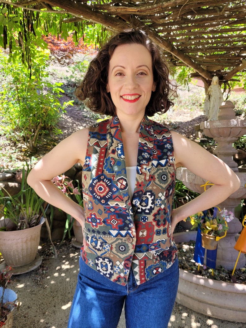 May include: A sleeveless vest with a colorful geometric pattern in shades of red, blue, green, and brown. The vest has a button closure and a collar.