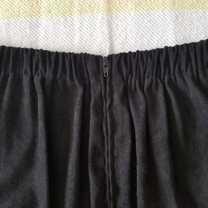 May include: Black skirt with a zipper closure at the back. The skirt has a waistband with elastic.