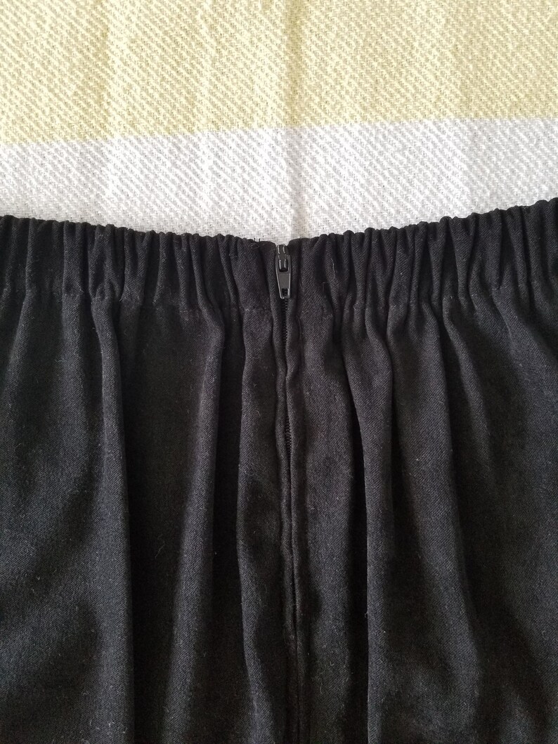 May include: Black skirt with a zipper closure at the back. The skirt has a waistband with elastic.