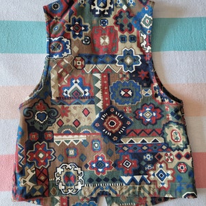 May include: A sleeveless vest with a geometric pattern in shades of brown, blue, red, and white. The vest has a collar and a button closure.