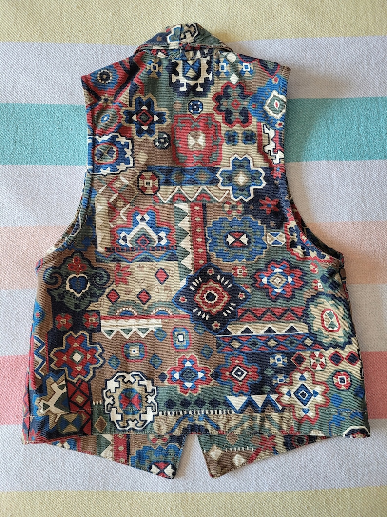 May include: A sleeveless vest with a geometric pattern in shades of brown, blue, red, and white. The vest has a collar and a button closure.