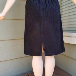 May include: A black skirt with an elastic waistband and a back slit. The skirt is made of a soft, textured fabric.