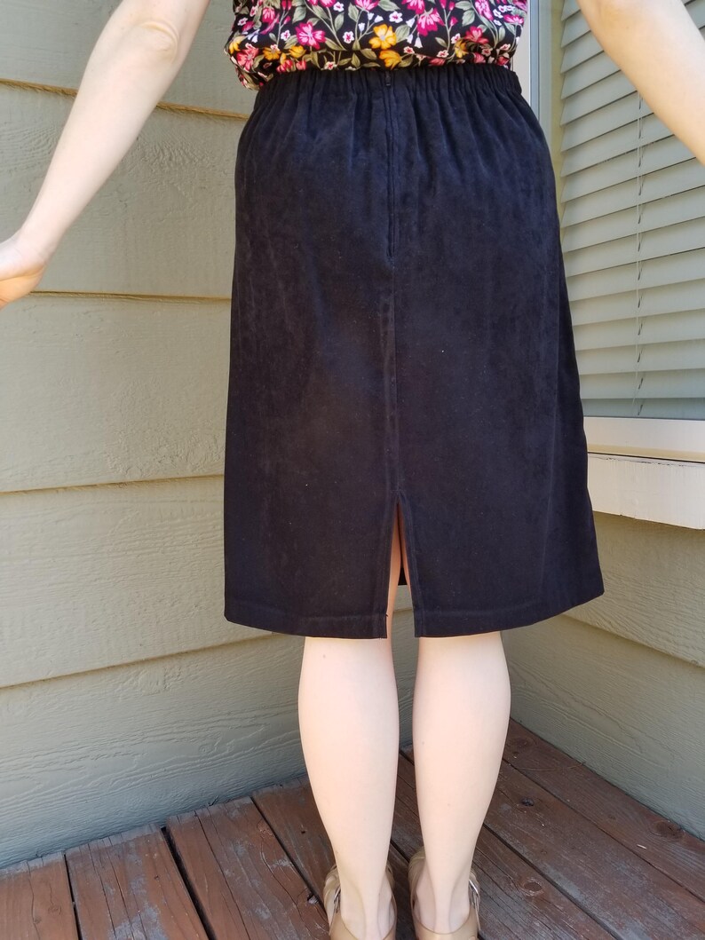 May include: A black skirt with an elastic waistband and a back slit. The skirt is made of a soft, textured fabric.