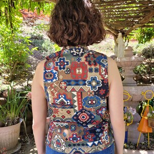 May include: A sleeveless vest with a geometric pattern in shades of brown, blue, red, and white. The vest is made of a woven fabric and has a relaxed fit.