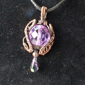 May include: A handcrafted pendant necklace featuring a faceted, light purple crystal orb, wire-wrapped in copper. A teardrop-shaped crystal hangs below the orb. The pendant is suspended from a black cord.