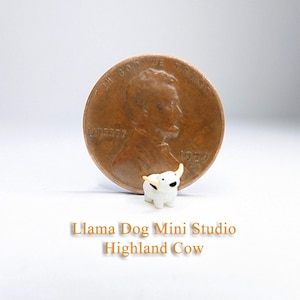 May include: A small white Highland Cow figurine with brown horns, next to a US penny for scale. Llama Dog Mini Studio Highland Cow.