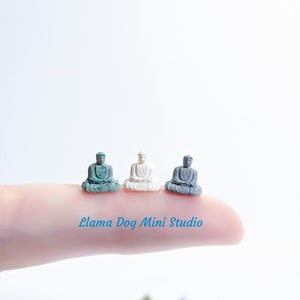 May include: Three miniature Buddha statues in different colours: green, white and grey. The statues are sitting in a meditative pose with their hands in their laps.