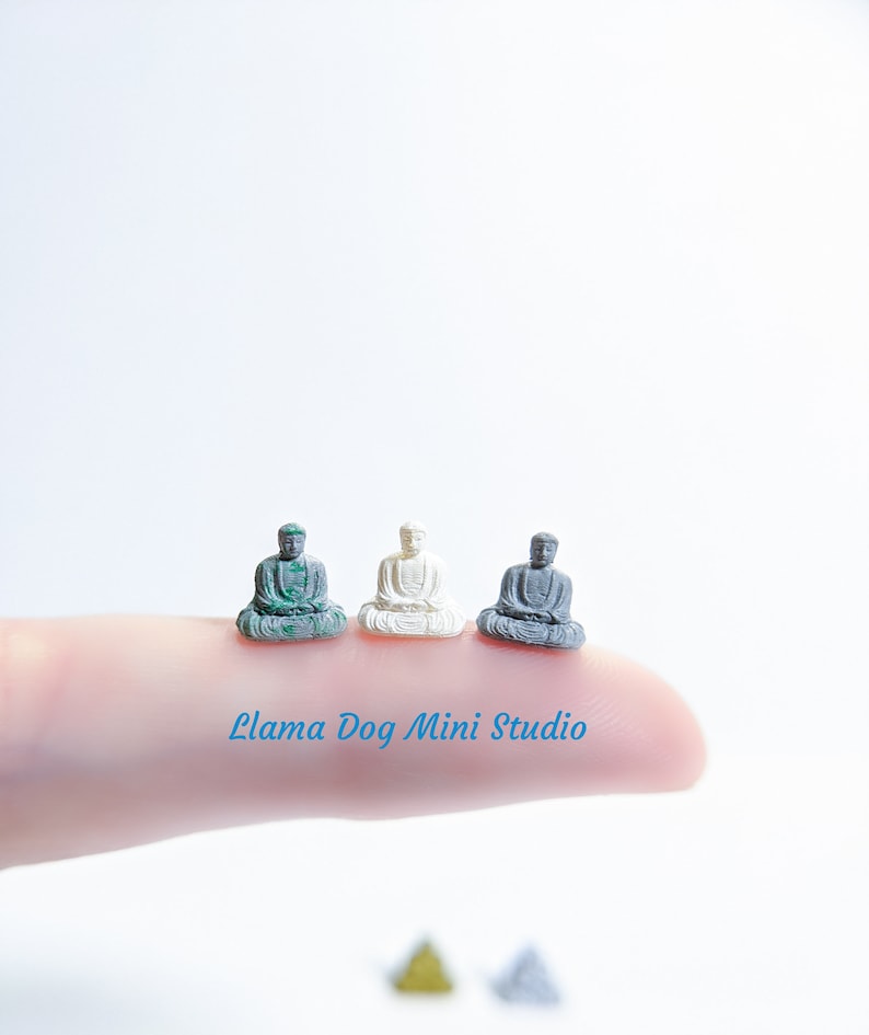 May include: Three miniature Buddha statues in different colours: green, white and grey. The statues are sitting in a meditative pose with their hands in their laps.
