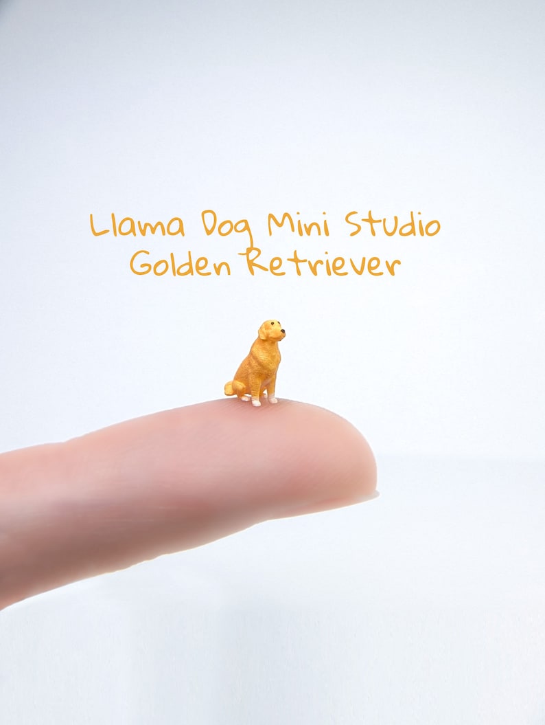 Puede incluir: Una figurita de golden retriever en miniatura, sentada en un dedo, con el texto "Llama Dog Mini Studio Golden Retriever" encima.