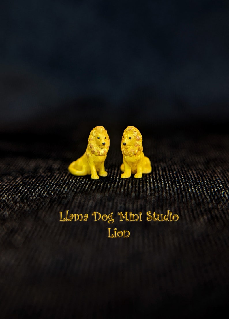 K&ouml;nnte beinhalten: Zwei kleine gelbe L&ouml;wenfiguren, die sich gegen&uuml;berstehen. Die Figuren sitzen auf einer schwarzen, strukturierten Oberfl&auml;che. Der Text "Llama Dog Mini Studio Lion" befindet sich unter den Figuren.
