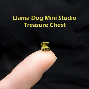 Może przedstawiać: Miniaturowa drewniana skrzynia skarbów z pozłacanym wiekiem i złotymi zdobieniami. Skrzynia jest otwarta i wydaje się być wypełniona złotymi monetami. Skrzynia leży na palcu.