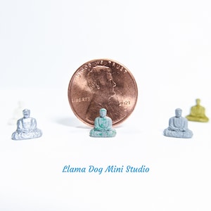 May include: Four miniature Buddha statues, one green, one silver, and two grey, are arranged on a white surface. A copper penny with the inscription "In God We Trust" and "Liberty" is in the centre of the image. The text "Llama Dog Mini Studio" is at the bottom of the image.