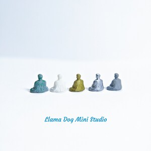 May include: Five miniature seated figures in different colours: teal, white, gold, silver, and grey. The figures are arranged in a row on a white surface. The text "Llama Dog Mini Studio" is printed below the figures.