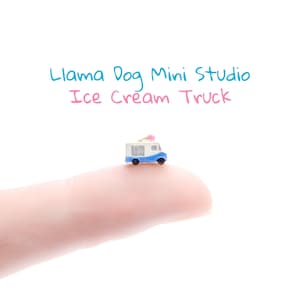 May include: A miniature blue and white ice cream truck with a pink ice cream cone on top, sitting on a finger.